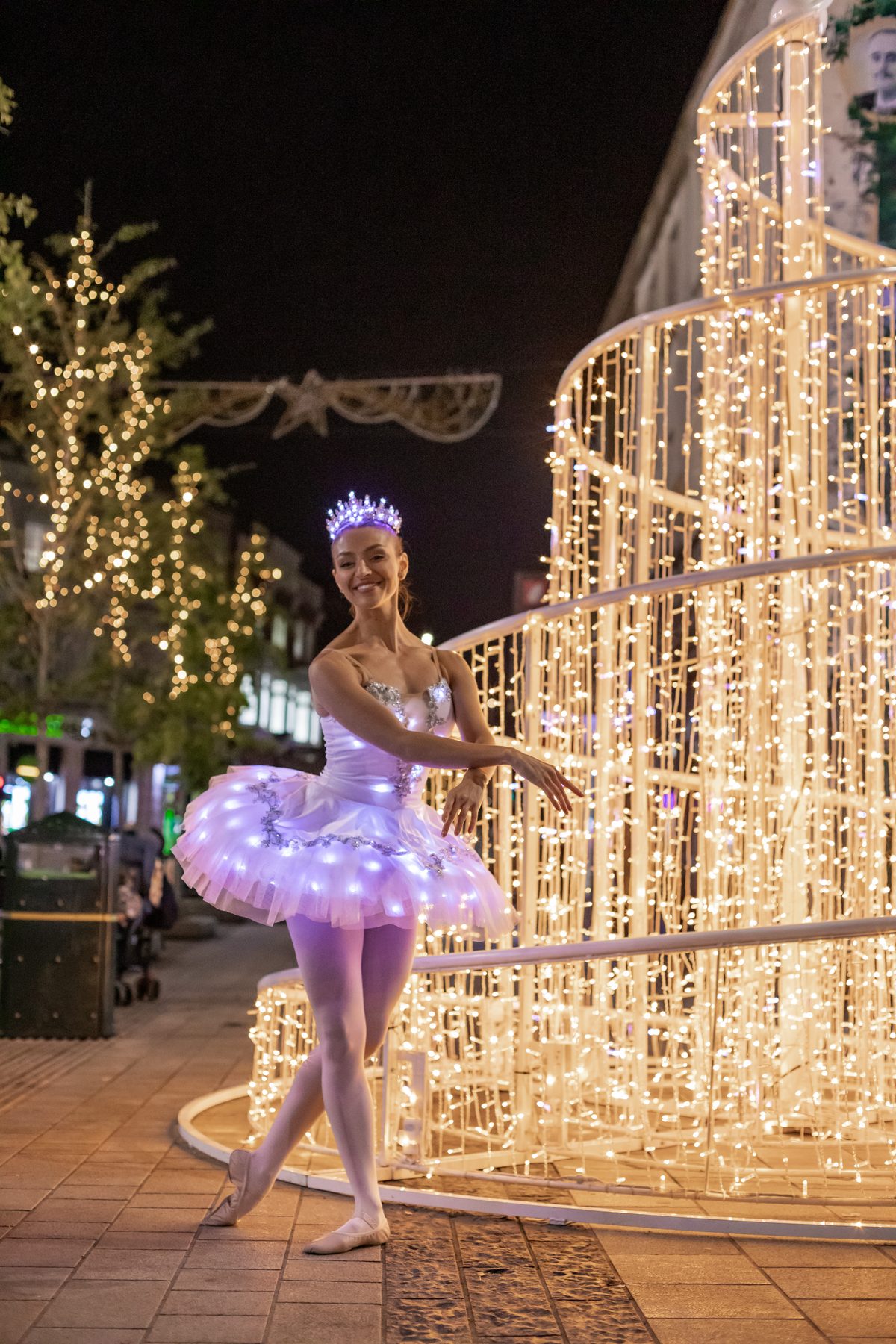 An illuminated ballerina beside a light installation at night